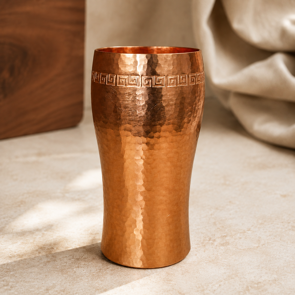 Hammered copper tumbler with Greek-key border on cream stone
