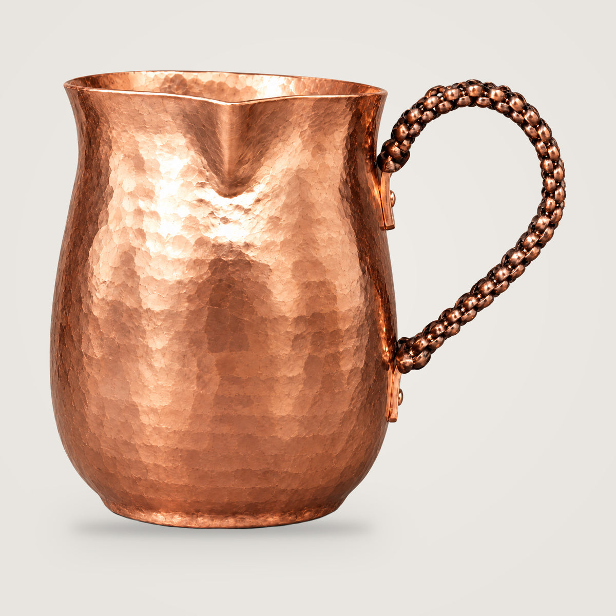 Hammered copper milk and coffee pot on a plain light grey background