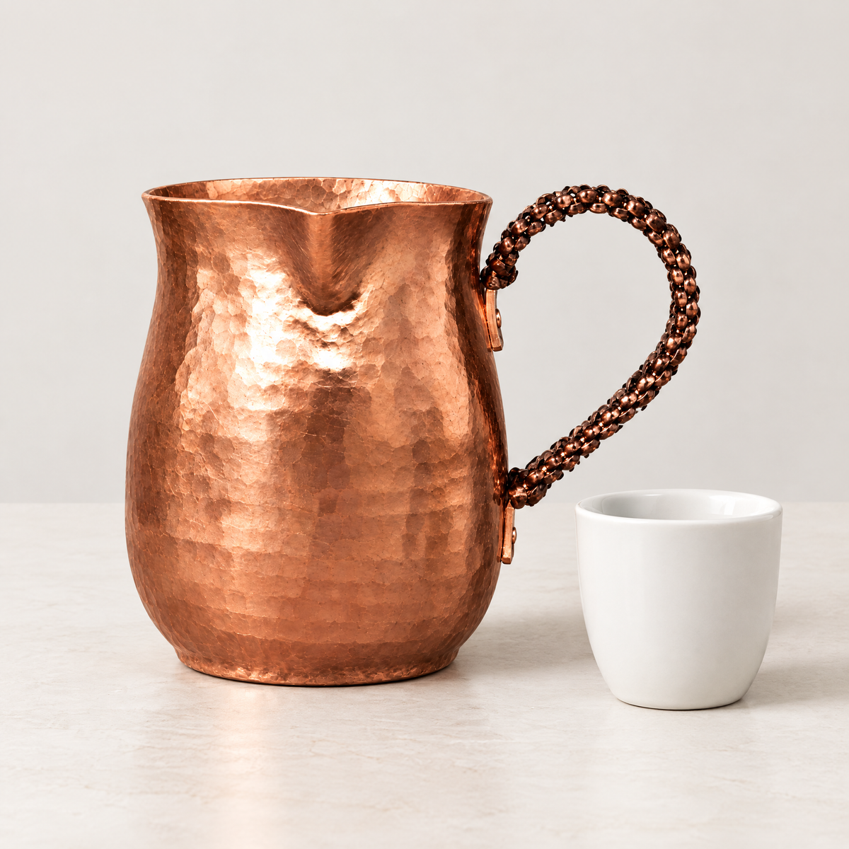 Copper coffee pot beside a small white ceramic cup