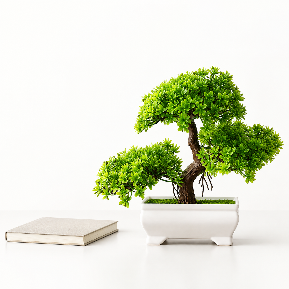 Artificial bonsai tree on a desk beside a notebook for scale